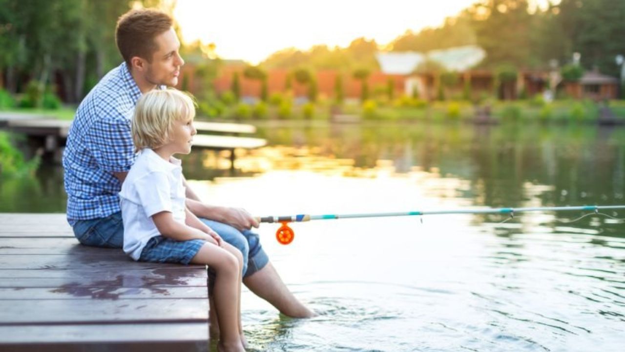 A family fishing together at a cabin pond with the Smoky Mountains in the background.